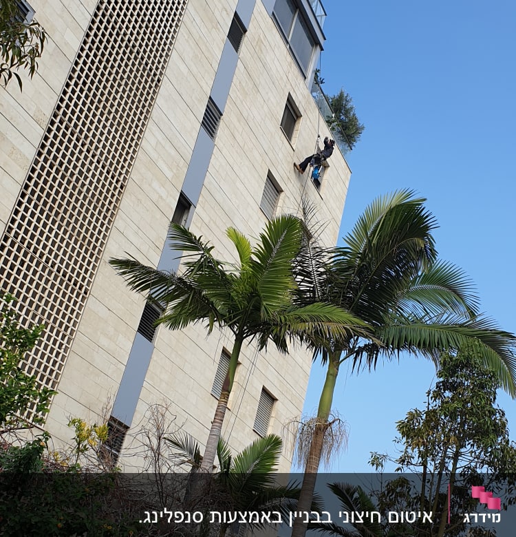 אדם תלוי על חבל מבצע עבודת איטום על קיר בניין